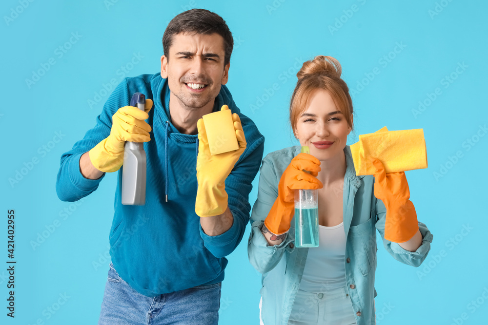 Young couple with cleaning supplies on color background Young couple with cleaning supplies on color background