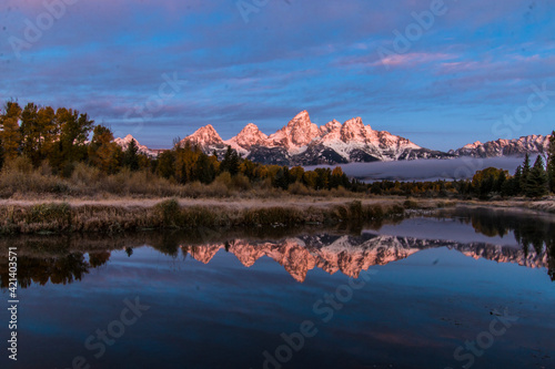 dramatic wintry autumn sunrise of the Grand Tetons mountain range and its reflection.