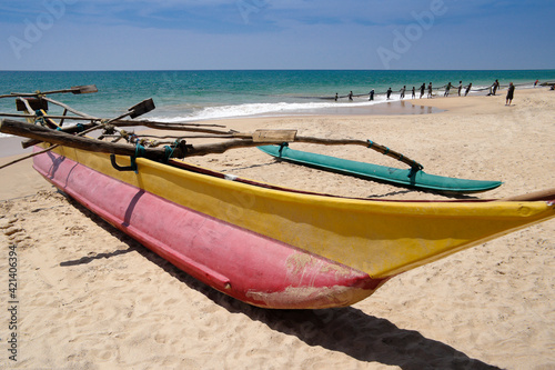 At Ambalangoda, Sri Lanka, a traditional outrigger sea canoe (oru) rests on the sand as fishermen in the background haul in their large net (madela).