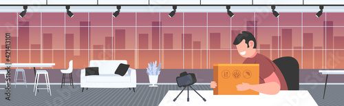 man blogger opening parcel box recording unboxing video with camera on tripod blogging mail delivery concept office interior horizontal portrait