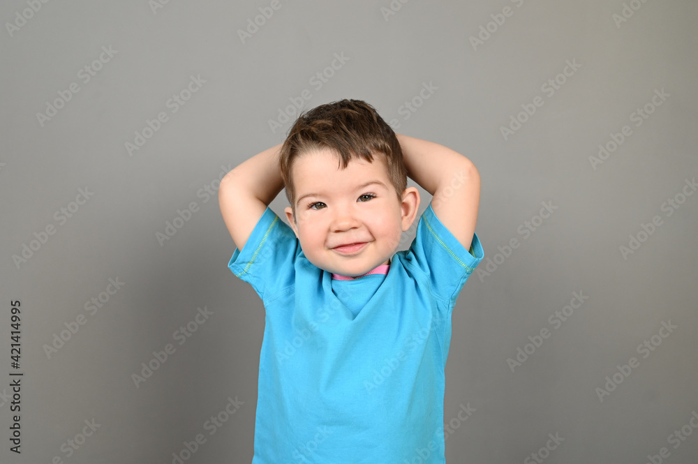 A smiling Caucasian boy in a blue T-shirt poses on a gray background. A smiling Caucasian boy in a blue T-shirt poses on a gray background.