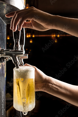 Photography Bartender hands pouring a cold draft beer into a mug , black background