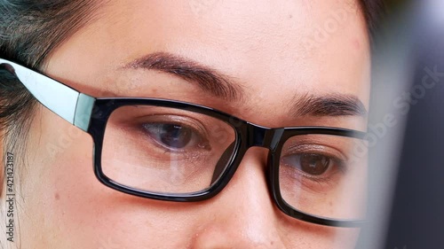 Close-up eyes of Asian woman with glasses working on a laptop computer in her office.