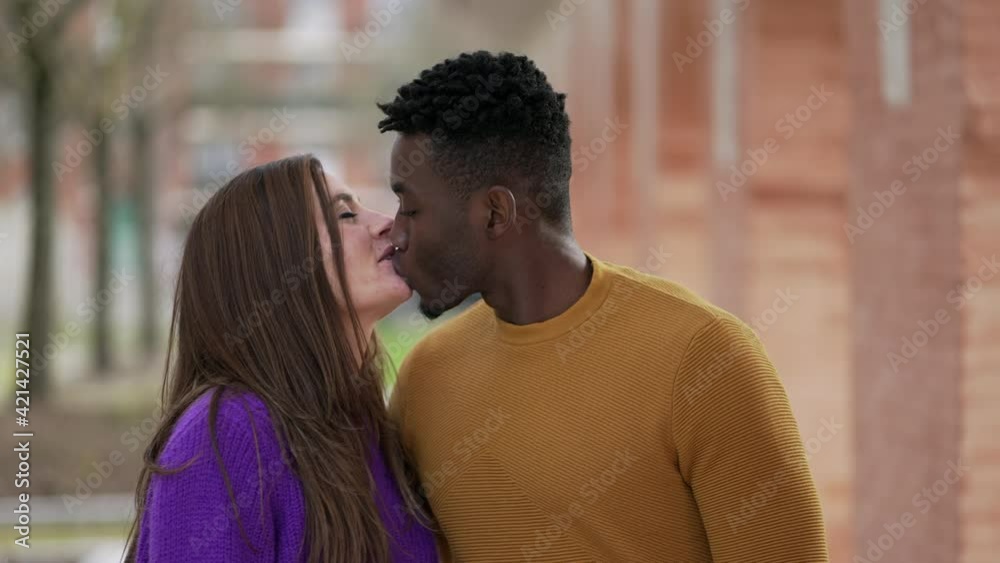 Young interracial couple kissing holding hands walking outside together Young interracial couple kissing holding hands walking outside together
