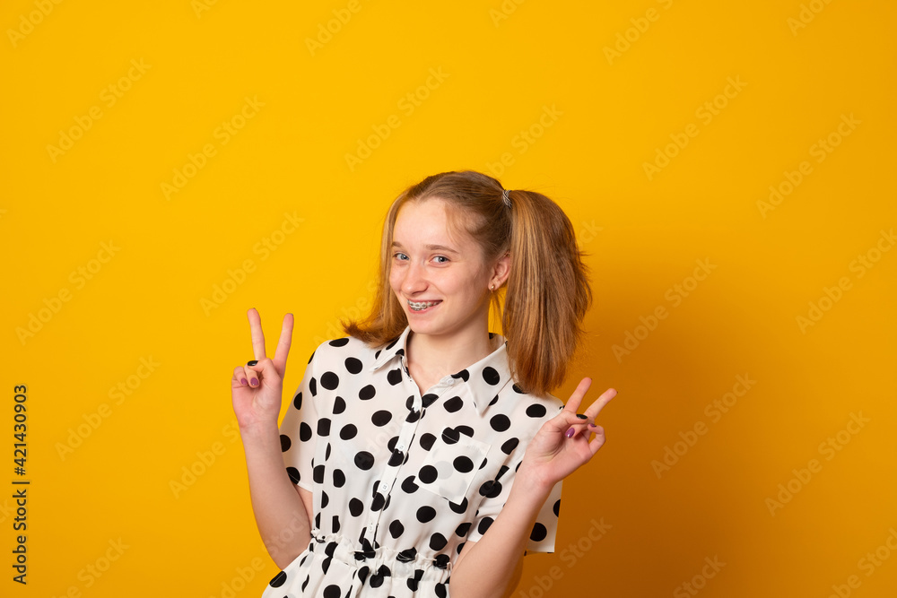 Funny teenage girl with a two-ponytail hairstyle smiles with braces grimaces and laughs on a yellow background.