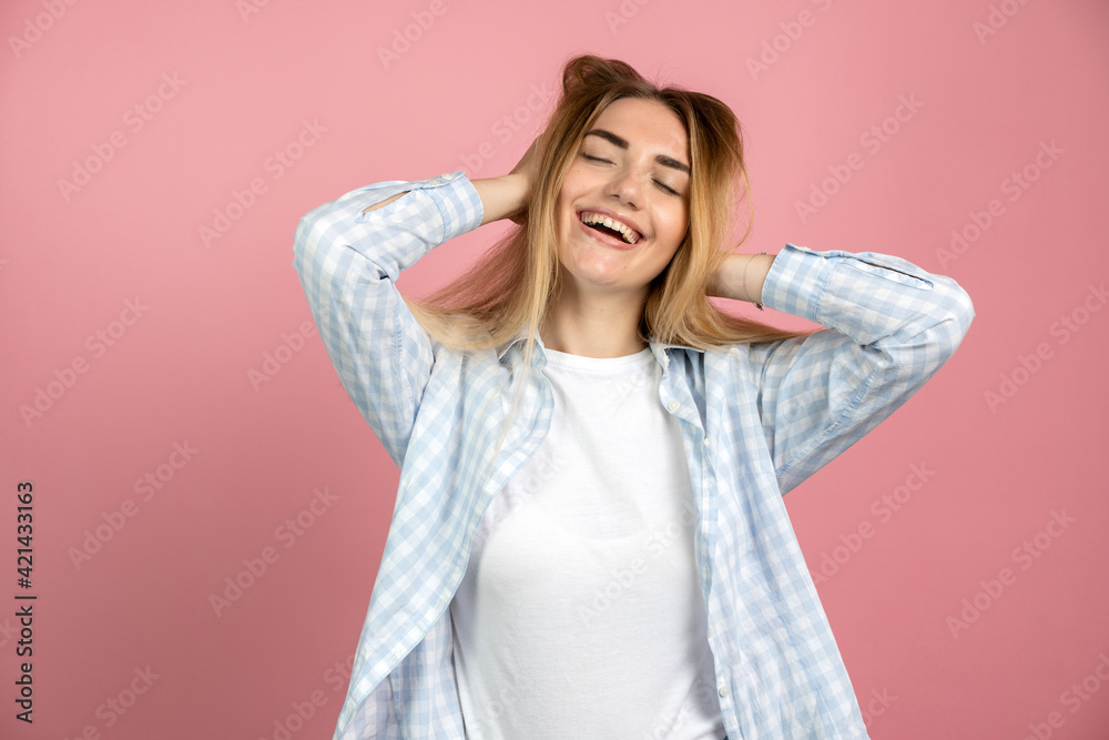 Happy, beautiful girl is smiling happily, touching her hair. Young girl posing on a background of a pink wall. Happy, beautiful girl is smiling happily, touching her hair. Young girl posing on a background of a pink wall.