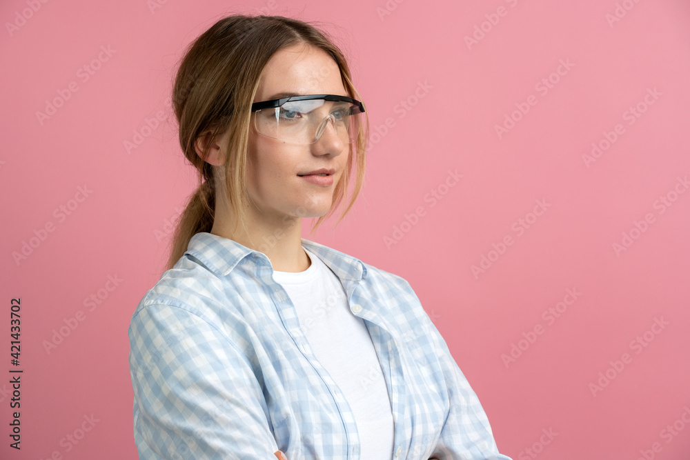 Serious woman construction worker on pink background for copy space. Young woman wearing safety glasses.