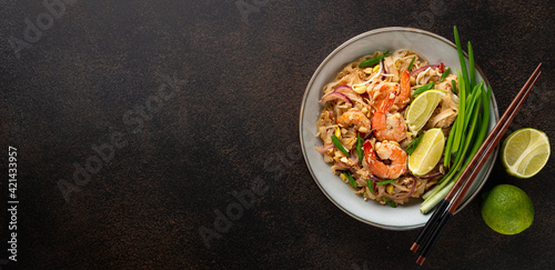 Pad Thai with shrimp in a ceramic bowl on a dark background, top view, copy space