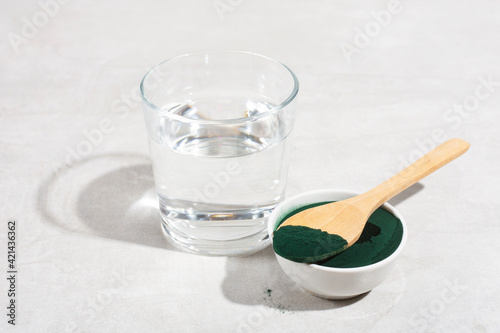 spirulina powder in a spoon on a gray table, glass of water