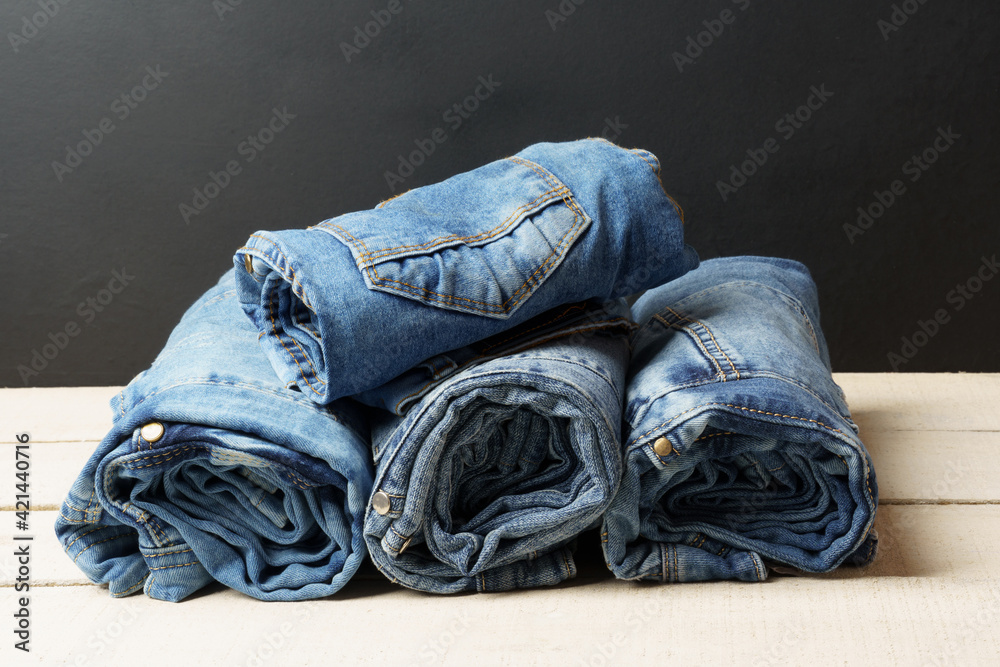 A stack of blue jeans on a wooden white table on a black
