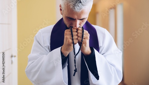 Hands of priest holding rosary and praying. photo