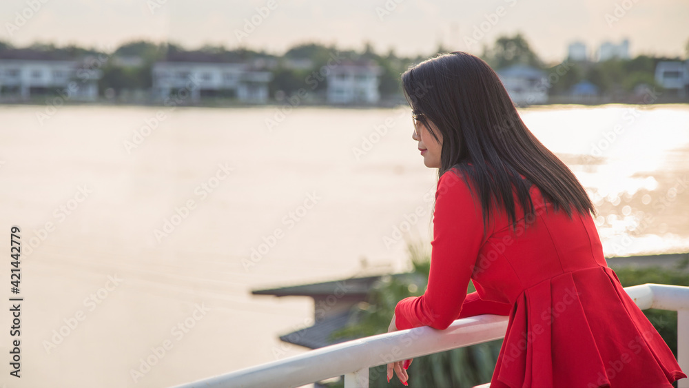 Portrait back Asian woman in a red formal suit wearing sunglasses looking away on the bridge with river background