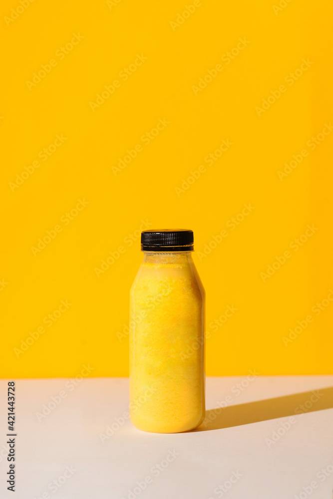 Smoothies of yellow color in a bottle on a yellow background with hard shadows. The concept of sports nutrition. Smoothies of yellow color in a bottle on a yellow background with hard shadows. The concept of sports nutrition.
