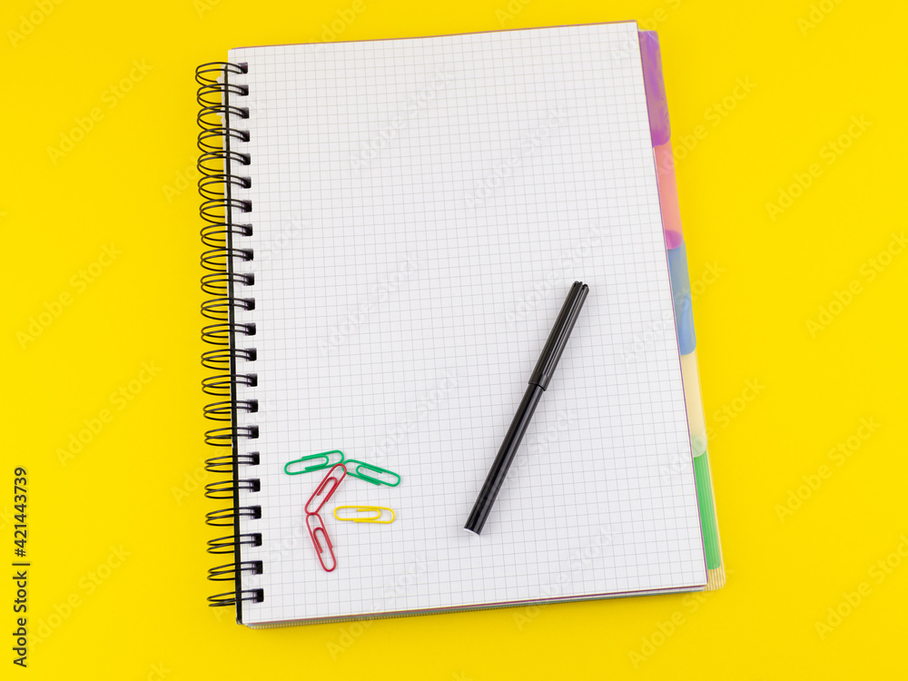 blank squared page on notepad, paper clips and felt-tip pen on yellow background blank squared page on notepad, paper clips and felt-tip pen on yellow background