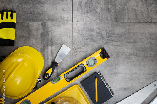 Contractor theme. Tool kit of the contractor: yellow hardhat, libella, hand saw. Plans and notebook on the gray tiles background. © zolnierek