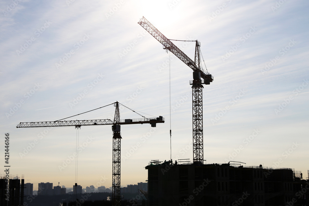 Construction cranes above the unfinished residential building against sunshine. Housing construction, apartment block in city Construction cranes above the unfinished residential building against sunshine. Housing construction, apartment block in city
