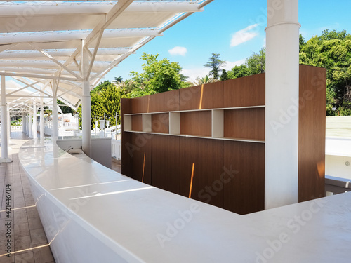 A summer bar with empty shelves and a white bar is located under a white canopy against a backdrop of green trees and palms photo