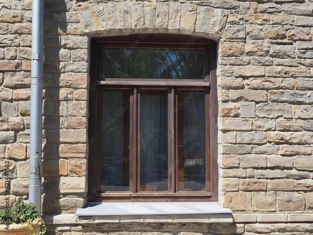 A brown framed window in a rough masonry wall illuminated by the sun A brown framed window in a rough masonry wall illuminated by the sun