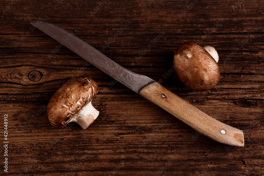 Cremini mushrooms and old kitchen knife on textured wooden table. Two baby portobello brown mushrooms. Closeup. Minimal style.