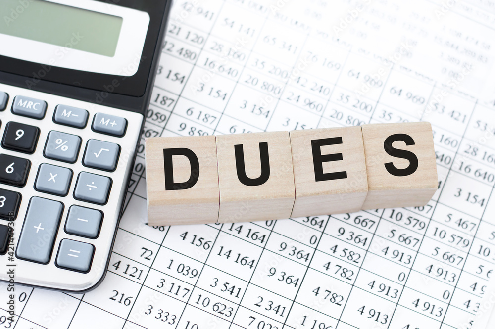 text Dues made with wood building blocks on the office table next to the calculator