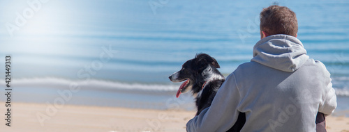 man sitting in front of the sea on the beach with his dog friend