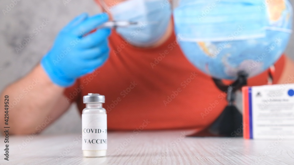 vial with a vaccine against the coronavirus, in the background a man is vaccinating the planet, the globe. Corona virus treatment concept, injection during a pandemic. Travel concept during a pandemic