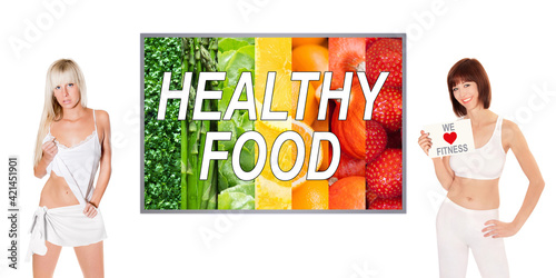 Two beautiful young women in front of a colorful photo with fruits and vegetables, healthy food is written on the image, one woman holding a paper, we love fitness is written on the poster  photo