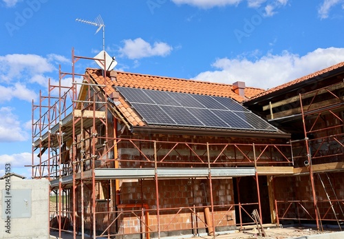 Solar panels already installed on the roof of a house under construction covered with scaffolding and still exposed brick. © luca piccini basile