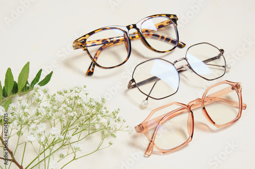 several fashionable glasses and flowers on a beige background copy space top view