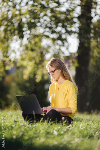 Adorable woman sitting on grass with laptop