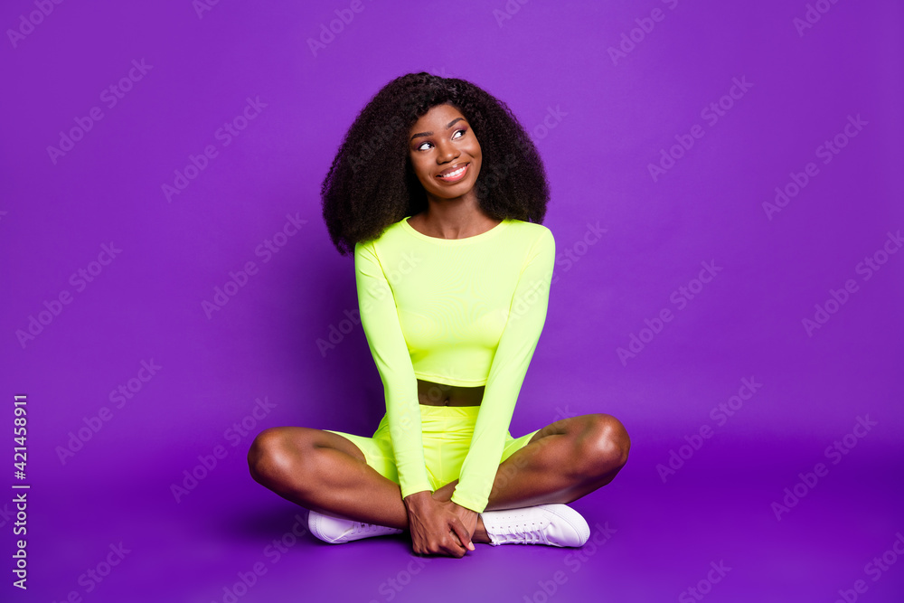 Full size photo of young charming smiling dreamy afro girl look copyspace sit floor isolated on violet color background Full size photo of young charming smiling dreamy afro girl look copyspace sit floor isolated on violet color background