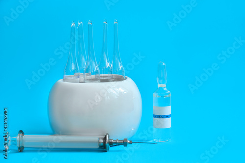 medicine in white round stand, syringe and free-standing glass ampoule on blue background