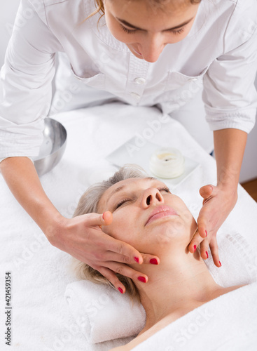 Aged smiling woman having professional face massage in spa salon