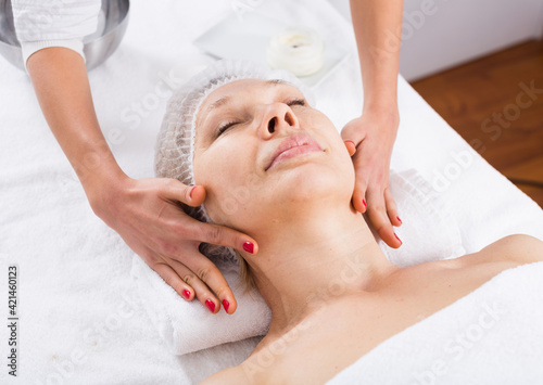 Aged smiling woman having professional face massage in spa salon