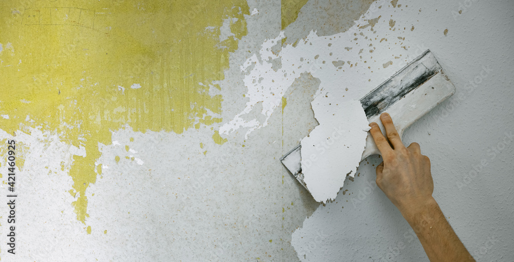 worker hand with scraper removing old wallpaper from the wall. house