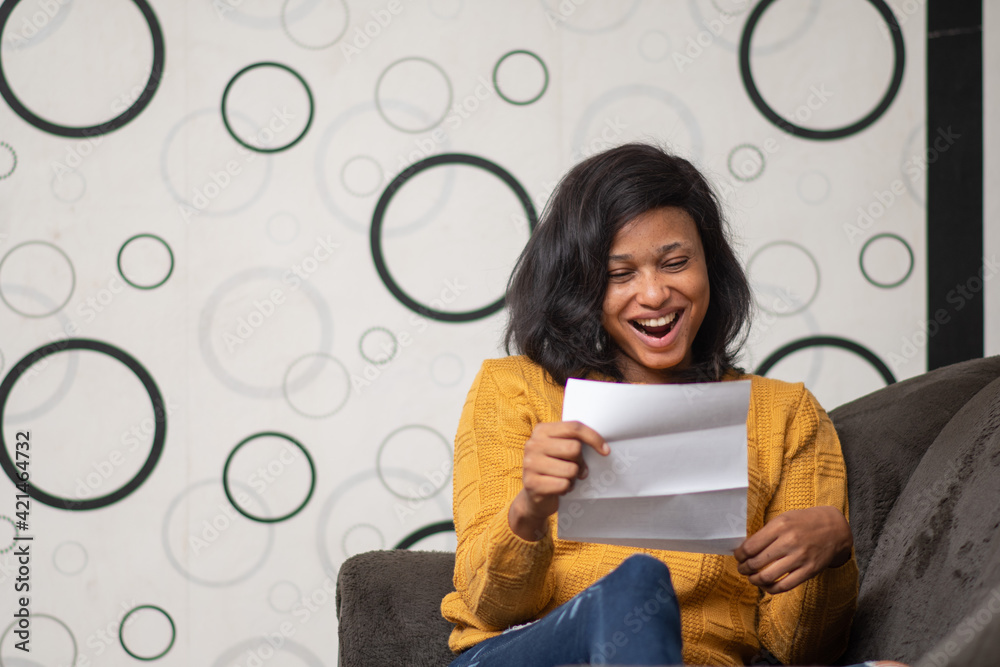 young black woman looks very happy reading a letter - obrazy, fototapety, plakaty 