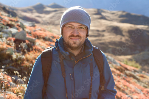 Trendy hipster portrait of man outdoor for healthy lifestyle design. Trekking of blogger photographer or vlogger with camera. Solo tourist in the Alps
