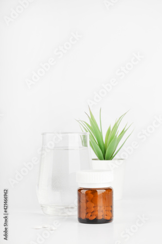 pills in glass bottle, green plant in pot and glass of water on white background. medicine and healthcare concept. copy space