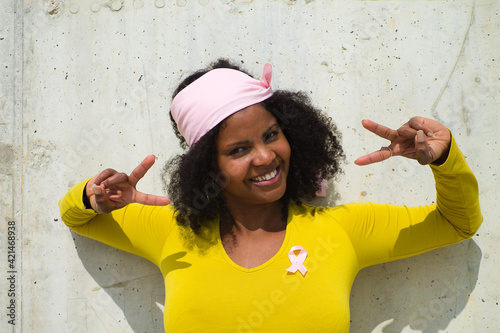 african-american woman with a pink scarf against the fight against breast cancer with a yellow t-shirt on grey background