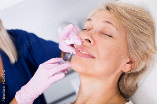 Mature female client receiving cosmetic injection from professional cosmetician