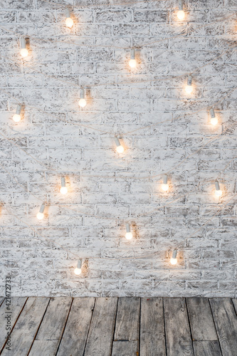 Light bulbs on white brick background with wooden floor. Vintage edison light bulbs garland in loft interior. Rustic Texture. Retro Whitewashed Old Brick Wall Surface. Design interior element