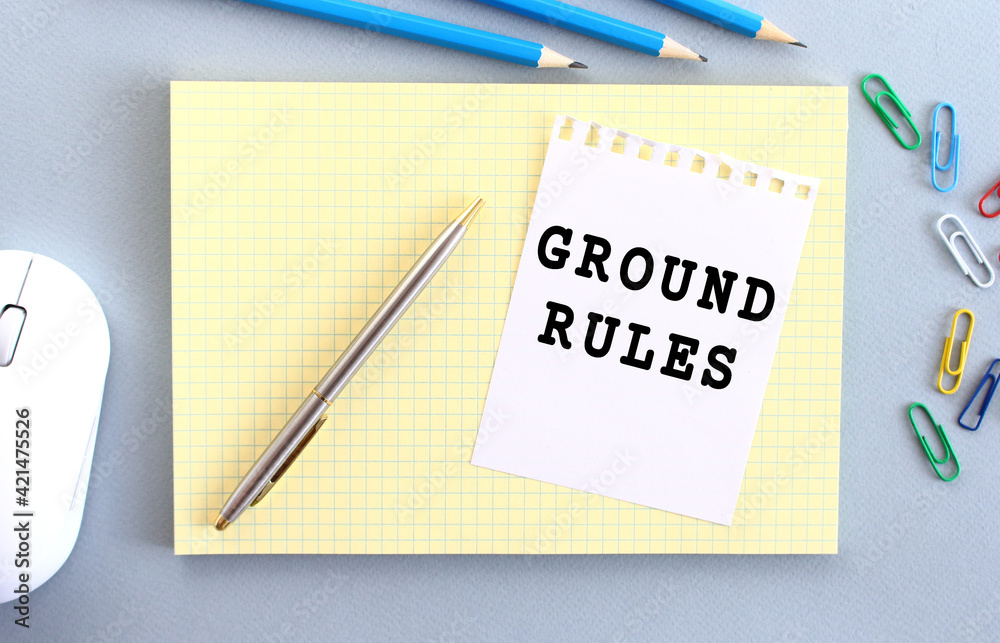 GROUND RULES is written on a piece of paper that lies on a notebook next to office supplies. GROUND RULES is written on a piece of paper that lies on a notebook next to office supplies.
