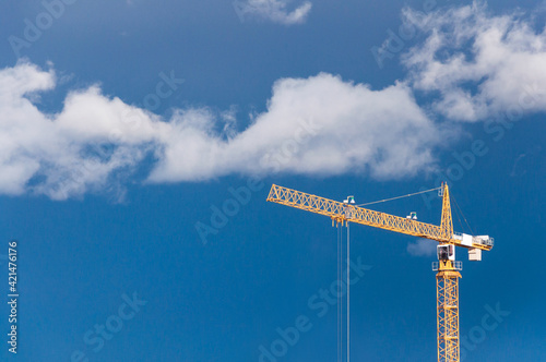 Yellow industrial construction tower crane against blue sky with clouds on the background, real estate building development, architecture business concept work