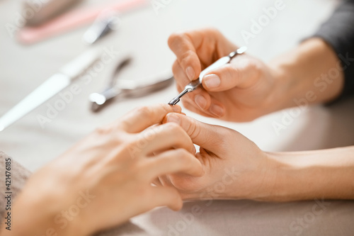 Beautician using cuticle pusher on woman hand photo