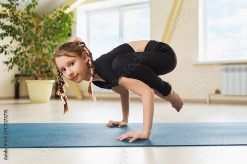 Obraz na plátne Little girl in black sportswear practicing yoga doing handstand exercise, kakasa