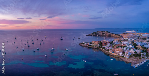 Amazing sunset in Ibiza Spain with orange and violet sky and boats floating on the sea and coast view of the town