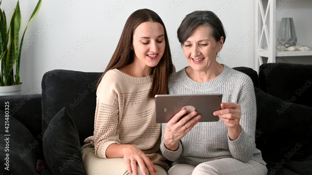 A senior mother and a grown daughter using a digital tablet for video call, two females different generation waving hands, greeting family online, staying in touch with relatives during quarantine A senior mother and a grown daughter using a digital tablet for video call, two females different generation waving hands, greeting family online, staying in touch with relatives during quarantine