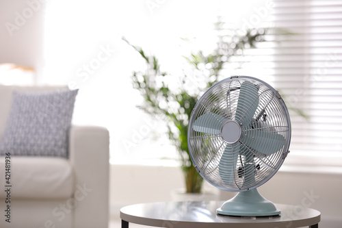 Modern electric fan on white table in living room. Space for text
