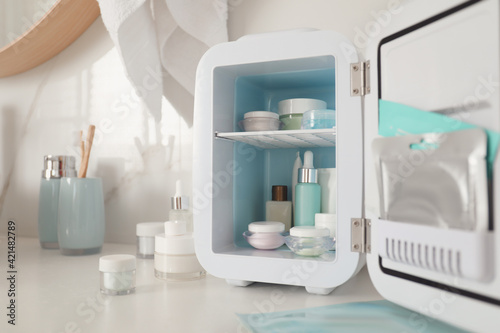 Cosmetics refrigerator and skin care products on white table indoors  closeup