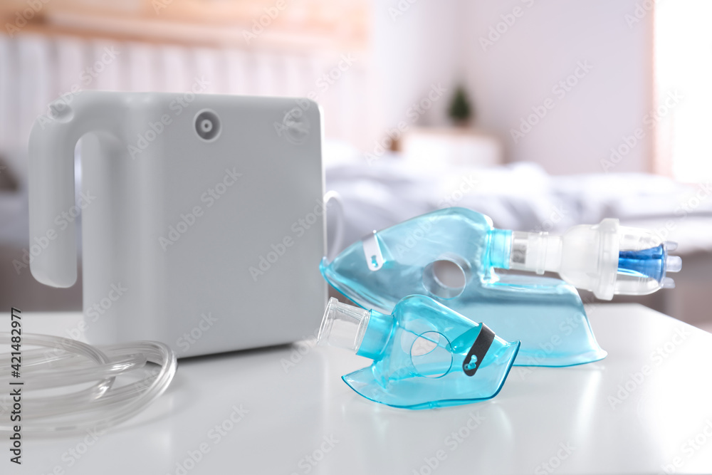 Modern nebulizer with face masks on white table indoors. Equipment for inhalation Modern nebulizer with face masks on white table indoors. Equipment for inhalation